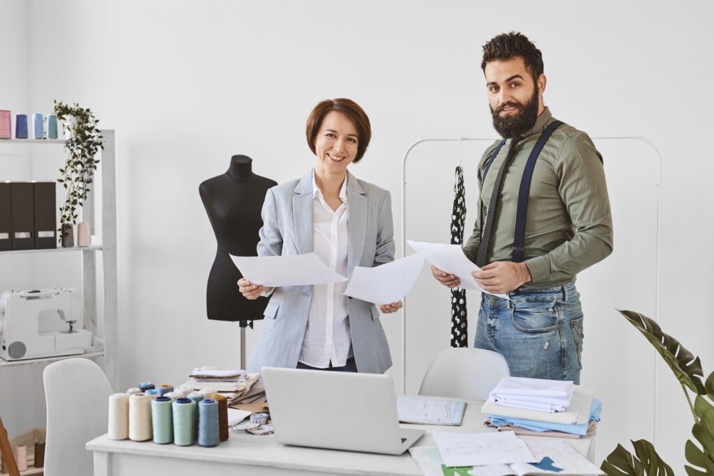 two fashion designers posing atelier with clothing line plans.